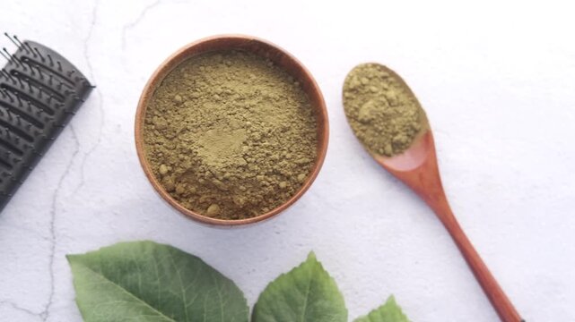 Overhead shot of henna powder in wooden bowl and spoon with hair comb and leaves