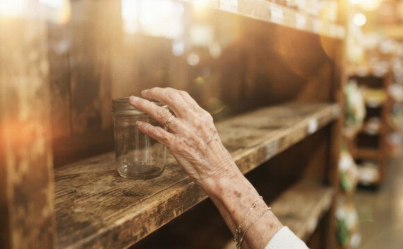 Elderly woman hand touching glass jar on store shelf representing shopping and memory