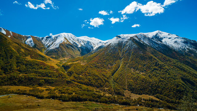 Panoramic view of snow-capped Caucasus Mountains from Chkhutnieri Pass in Svaneti, Georgia, surrounded by autumn vegetation and alpine valleys.