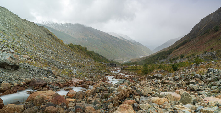 Landscape photograph of rocky mountain stream flowing through autumn valley under overcast sky in Svaneti Georgia.