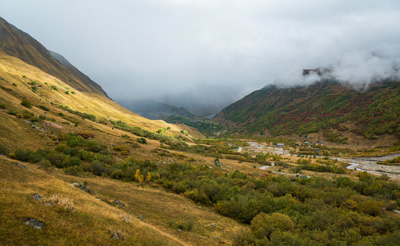 Landscape photograph of autumn mountain valley with river and clouds rolling over hills in Svaneti Georgia.