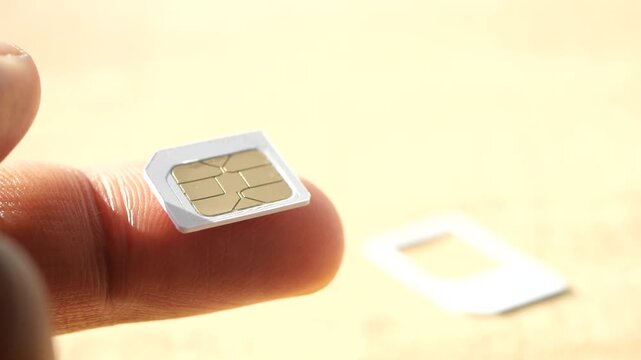 A close up view of person holding a micro SIM card between fingers, with a light background and a SIM card adapter in the background