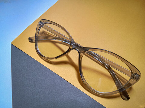 Close up of transparent cat eye eyeglasses frame on two tone yellow and grey background in high angle view