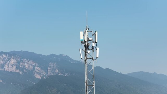 Communication base station tower with antennas against blue sky and distant mountains
