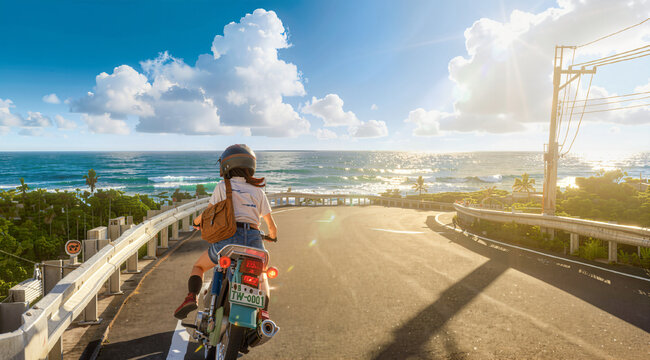 The a rider on a scooter journeys along a scenic coastal highway with a stunning view of the bright ocean and blue sky.