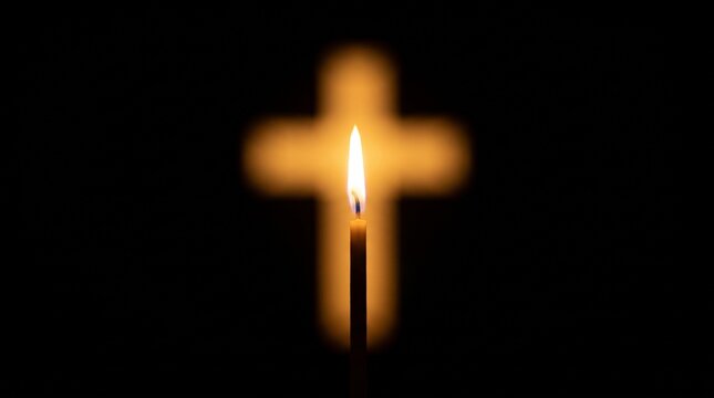 A single lit candle burning in front of a glowing blurred cross symbol on a black background with focus cross dark
