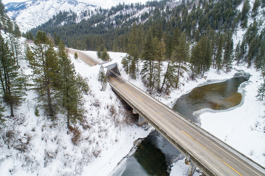 Winter road bridge over river surrounded by snow-covered pine trees