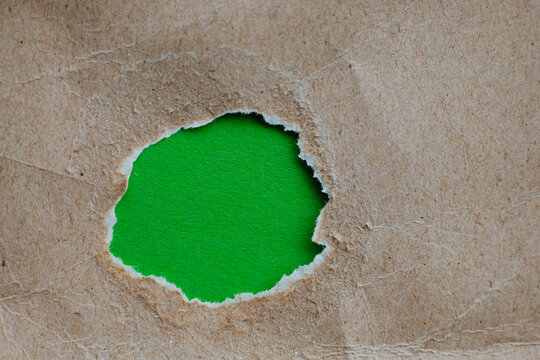  torn hole in kraft paper revealing green background for teaser campaigns, hidden messages, investigations concepts. 