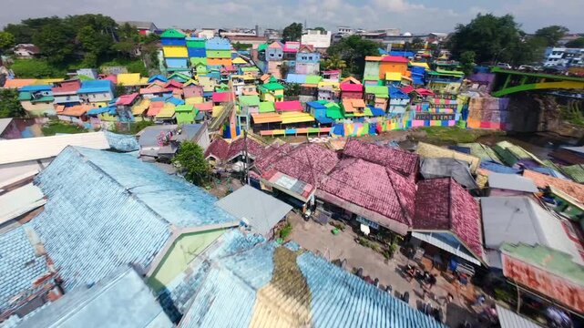 Dynamic FPV drone flight over railway tracks and colorful houses of Jodipan Village in Malang, Indonesia, revealing the vibrant riverside neighborhood and painted rooftops of East Java.