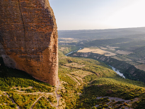 Aerial view of a giant rock tower of the Mallos de Riglos above the green valley and the Gallego river in Aragon, Spain, an iconic geological landmark of the Spanish Pyrenees foothills.