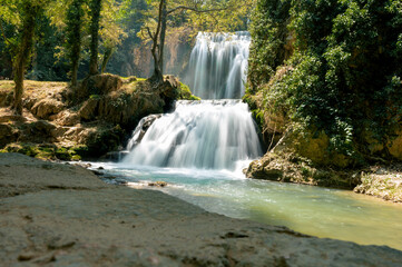 Obraz premium A waterfall cascades over rock ledges surrounded by greenery in the Monasterio de Piedra natural park in Aragon, Spain, a soft long exposure of silky white water and a turquoise pool.