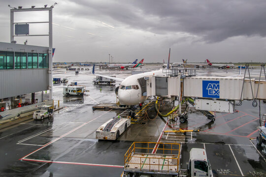 New York, NY - US - Sep 11, 2026 : A Delta Air Lines plane sits parked on a wet tarmac connected to an American Express jet bridge at John F. Kennedy International Airport, with ground service trucks.
