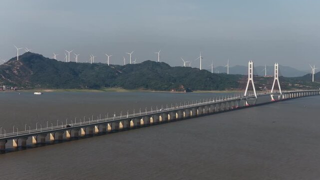 Cross sea bridge connecting green mountains and wind power farm