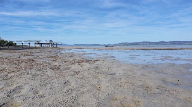 Timelapse of extreme low water at Lake Balaton, Hungary. Dry sandy lakebed with incoming shallow water, a pier, and boat showing drought.