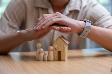 Hands sheltering wooden house and family figure, symbolizing home protection, security, care,...