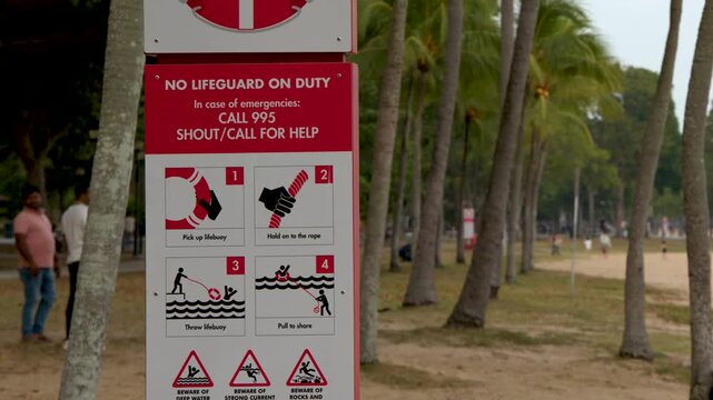 Red warning sign at beach showing no lifeguard on duty with emergency instructions and safety icons.