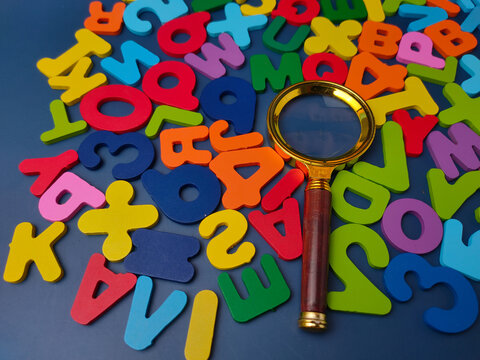 A brass magnifying glass lies across a scattered arrangement of colorful wooden alphabet letters and numbers