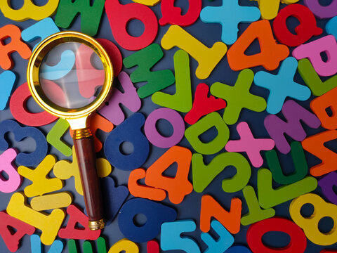 A brass magnifying glass rests directly over a dense spread of colorful wooden alphabet letters and numbers
