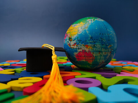 A miniature globe and a black graduation cap rest together on scattered colorful wooden letters and numbers