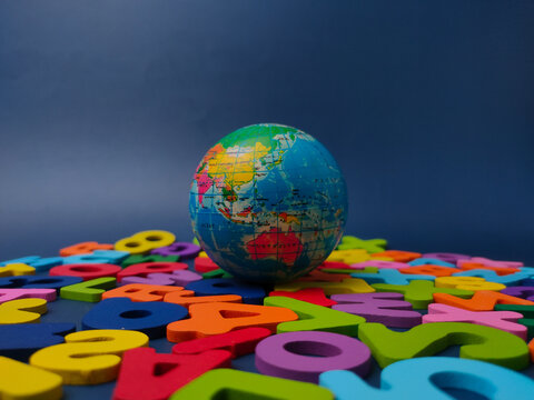 A small globe sits centered amidst a wide arrangement of colorful wooden letters and numbers on blue