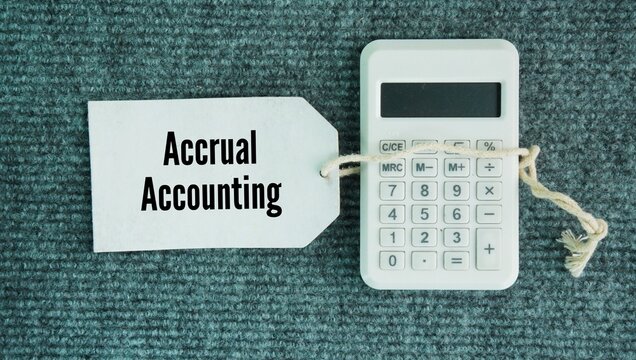 Calculator and paper tag with the word accrual accounting is the recording of revenue earned or an expense incurred before any cash actually changes hands.