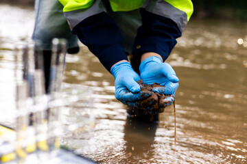 Field worker collecting muddy riverbed sediment to test for toxic pollutants and heavy metal...