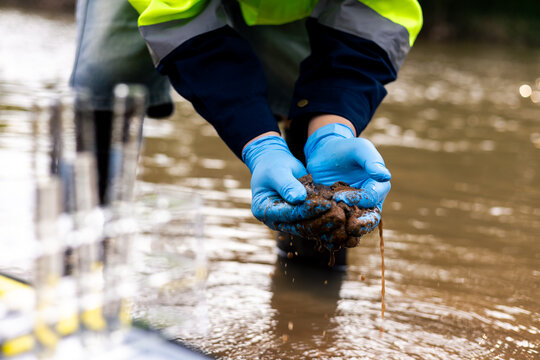 Field worker collecting muddy riverbed sediment to test for toxic pollutants and heavy metal contamination.