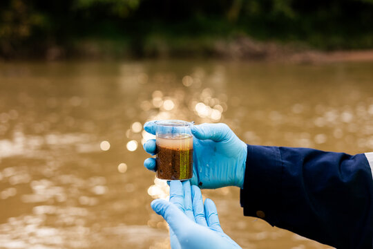 Environmental technician collecting river sediment sample for contaminant and heavy metal analysis.