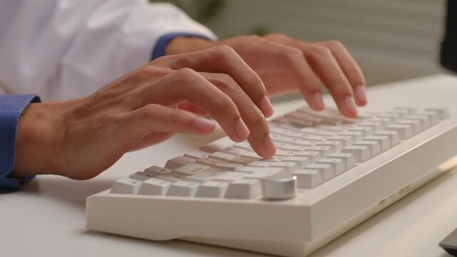 Doctor in white coat typing on computer keyboard to enter electronic medical health records in hospital office