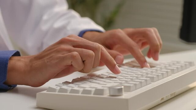 Doctor in white coat typing on computer keyboard to enter electronic medical health records in hospital office