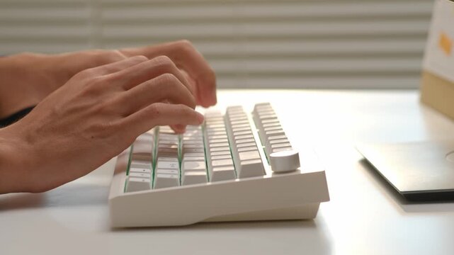 Close-up of professional hands typing on mechanical keyboard while working at office desk near window