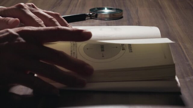 Finger tracing lines of text in open book beside round metal object