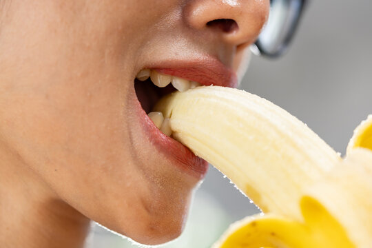 Close up mouth eating peeled banana with visible teeth and glasses, healthy snack captured in colorful detail for nutrition and lifestyle concept