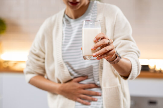 Woman holding milk glass while touching stomach with discomfort at home, suggesting digestive sensitivity, lactose intolerance, abdominal pain, and nutrition concern