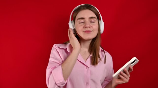  woman enjoys listening to music in studio on red background. Headphones,sound and relax while listening to radio, streaming and joy. 