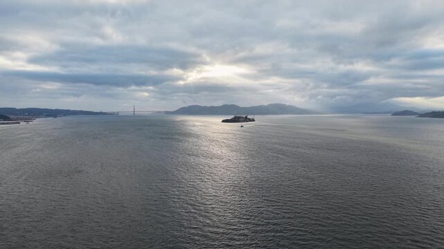 Aerial drone shot moving forward and rising over a local ferry boat, revealing Alcatraz Island and the distant Golden Gate Bridge in San Francisco
