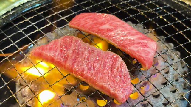 Premium raw wagyu beef grilling on charcoal barbecue with flames in Japanese restaurant style.