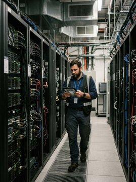 Male technician walking through server aisle while checking tablet