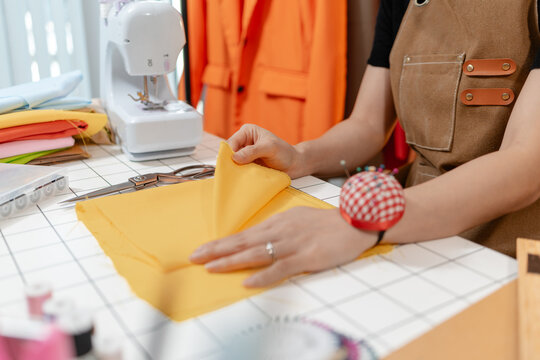 Professional fashion designer working in a modern sewing studio, measuring, marking and cutting fabric patterns for custom clothing production. Creative apparel development