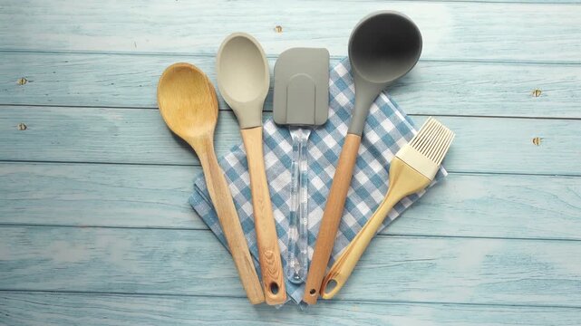 Top view of kitchen utensils set on blue wooden background with checkered napkin including spoon ladle and spatula