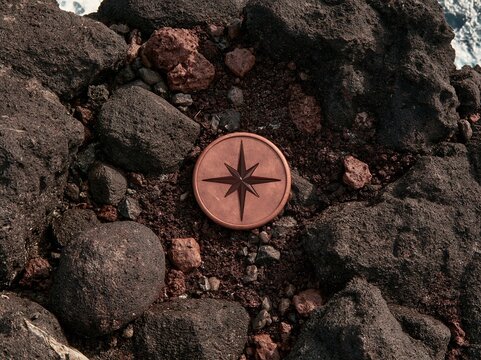 Copper compass rose navigation symbol placed on rough dark brown volcanic rocks at coastal shore adventure exploration travel direction finding natural concept