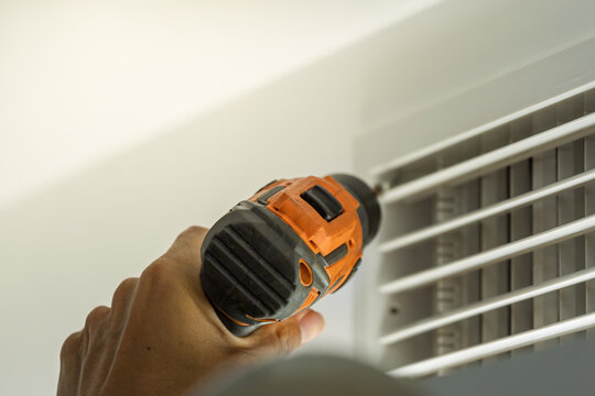 Worker using electric drill to disassemble central air conditioner for cleaning maintenance