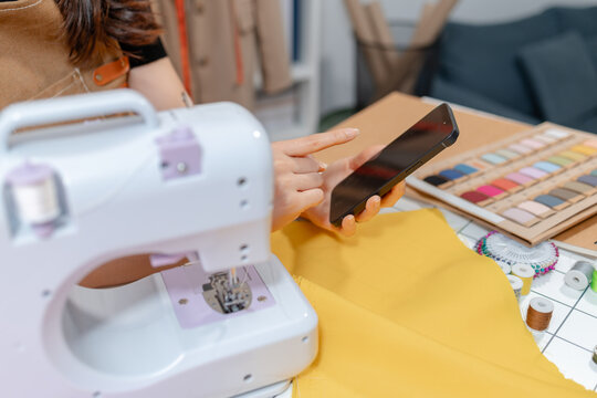 Professional fashion designer using a sewing machine in a modern studio while managing creative apparel production. Handmade craftsmanship, tailoring and small business workflow.