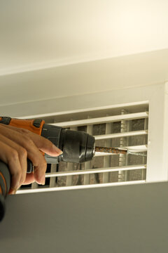 worker using electric drill to disassemble central air conditioner vent for cleaning maintenance