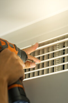 Worker dismantling central air conditioning vent to perform maintenance work