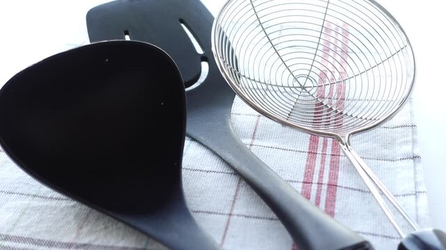 Kitchen utensils set with black spatula and metal strainer on checkered napkin for culinary cooking preparation footage