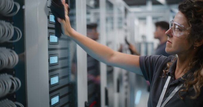 IT Maintenance Team Works in High Tech Server Corridor. Female Technician Sanitizes Glass Rack Doors With Spray Cleaner While Male Technician Operates Vacuum. Comprehensive Facility Upkeep Concept.