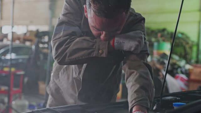 Mechanic repairing electric vehicle inside smoky garage workshop, performing engine maintenance near open hood while wearing protective workwear and gloves, focused automobile repair service during
