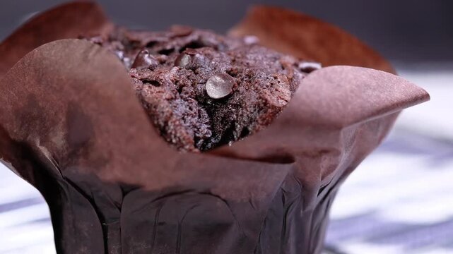 Freshly baked chocolate muffin with sweet chips in brown paper wrap cinematic macro video