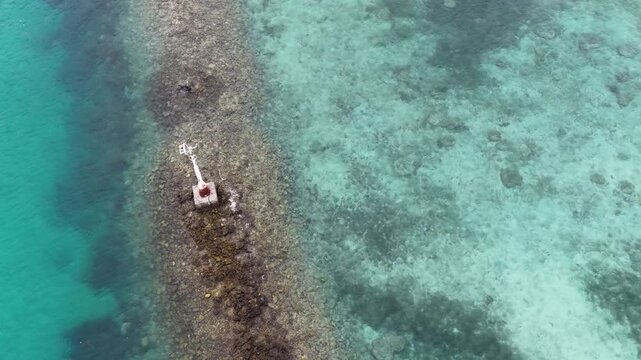 Aerial view of a weathered navigation marker on a submerged coral reef in clear turquoise water.